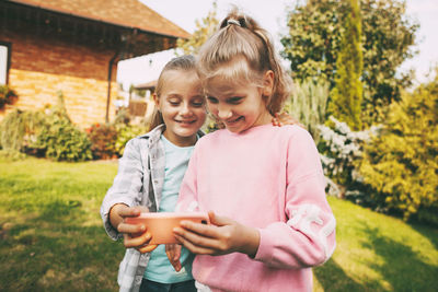 Two little girls outside their house are talking on a mobile phone with friends 