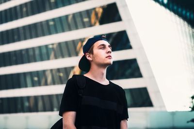 Low angle view of thoughtful man standing against building in city