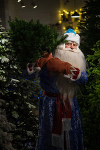 Portrait of santa clause standing amidst christmas tree