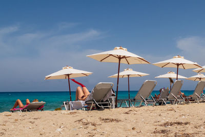 Lounge chairs and parasols on beach against sky