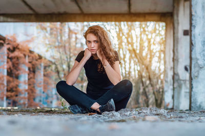 Teenage girl sits cross-legged, supports head with fists, legs crossed. evil look of blue eyes.