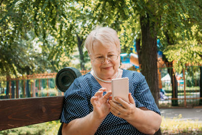 Young woman using smart phone while standing on tree