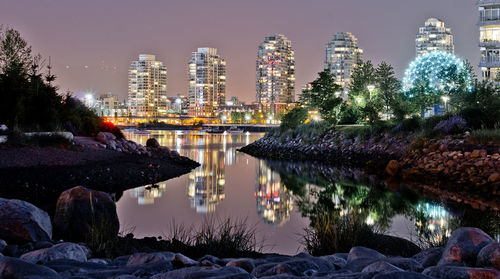 Illuminated cityscape by trees against sky at night