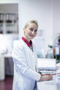 Smiling scientist standing by desk at laboratory