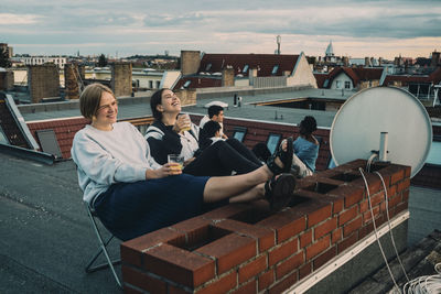 People sitting on roof against sky in city