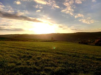 Scenic view of grassy field against sky at sunset