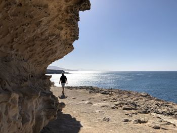 Man standing on rock by sea against sky