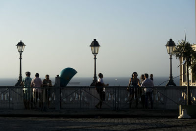 People on street against clear sky during sunset