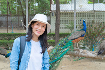 Portrait of smiling woman wearing hat with peacock at background