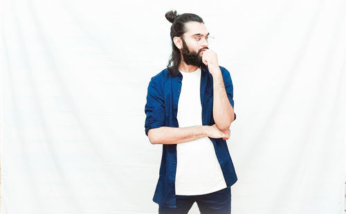 Young man looking away while standing against wall