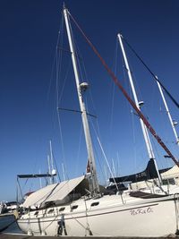 Low angle view of sailboats moored at harbor against clear blue sky