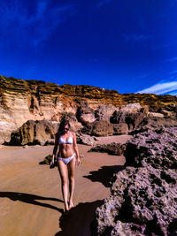 Young woman wearing bikini while walking at beach against sky during summer