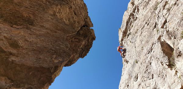 Low angle view of woman climbing rock against clear sky