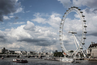 Ferris wheel in city against cloudy sky