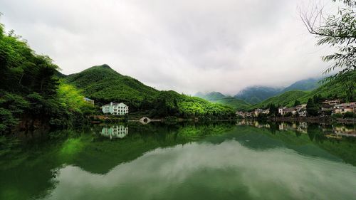 Scenic view of green hills by lake during foggy weather