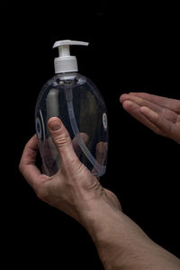 Midsection of man holding glass bottle against black background