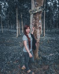 Portrait of smiling young woman standing amidst trees in forest