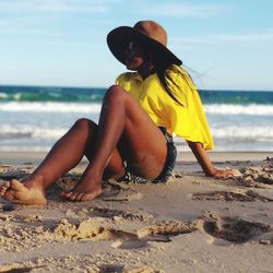 Brunette woman sitting on the beach sand over a blue sky