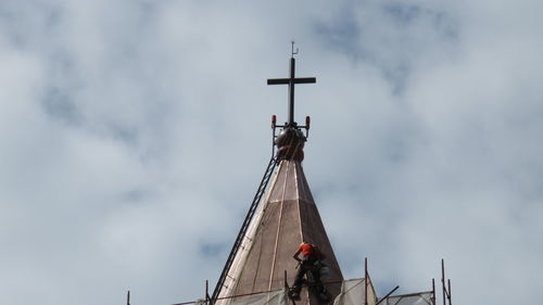 Low angle view of worker working on church steeple against cloudy sky