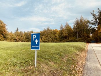 Road sign on field against sky