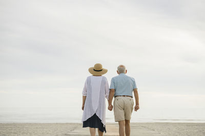 Back view of senior couple standing hand in hand on wooden boardwalk looking to the sea, liepaja, latvia