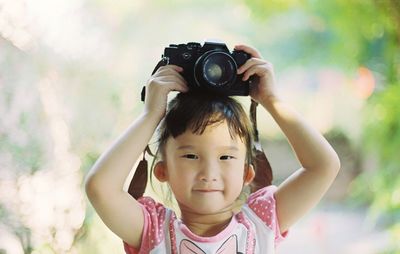 Portrait of girl photographing with camera while standing outdoors