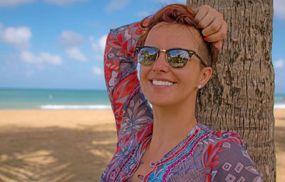 Portrait of smiling young woman standing at beach against sky