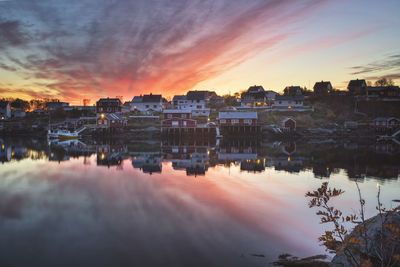 Scenic view of river by buildings against sky during sunset