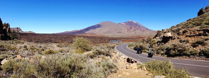 Scenic view of road by mountains against clear blue sky