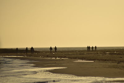 Silhouette people on beach against clear sky during sunset