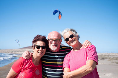 Portrait of happy friends standing at beach against clear sky