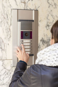 Rear view of woman using intercom on wall