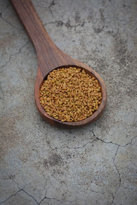 Fenugreek seeds in wooden spoon on cracked concrete texture background