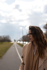 Young woman looking away while standing on road against sky