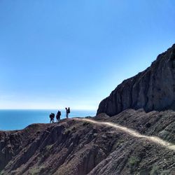 People hiking on mountain by sea against clear sky