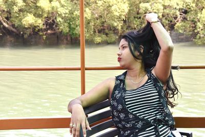 Young woman looking away while sitting on railing against sea