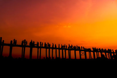 Silhouette people walking on wooden bridge during sunset