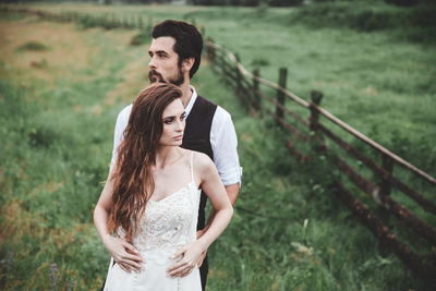 Wedding couple looking away while standing on field