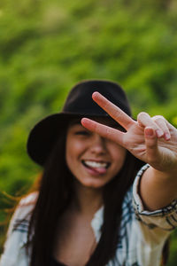 Portrait of young woman showing peace sign against plants