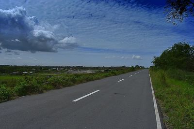 Country road amidst field against sky