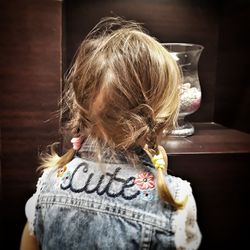 Rear view of girl with braided hair standing by shelf