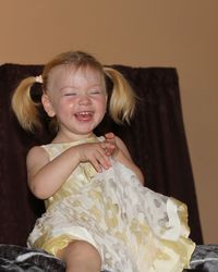 Cheerful girl laughing while sitting on chair by wall