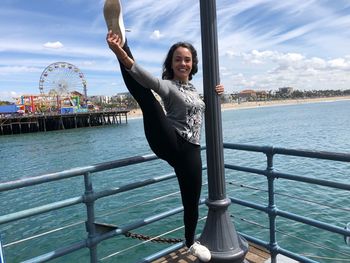 Portrait of smiling woman stretching while holding pole on pier in sea