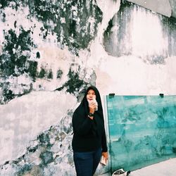 Portrait of young woman standing against built structure