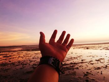 Midsection of person hand on sea during sunset