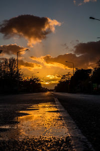 Wet road against sky during sunset