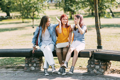 A group of teenage girls sitting and high-fiving with a laptop in the park. meeting on a training