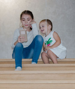 Siblings using mobile phone while sitting on staircase at home