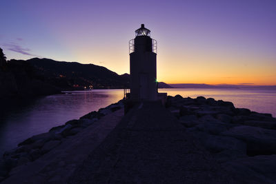 Lighthouse by sea against sky during sunset