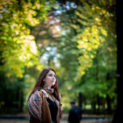 Portrait of young woman looking away against trees